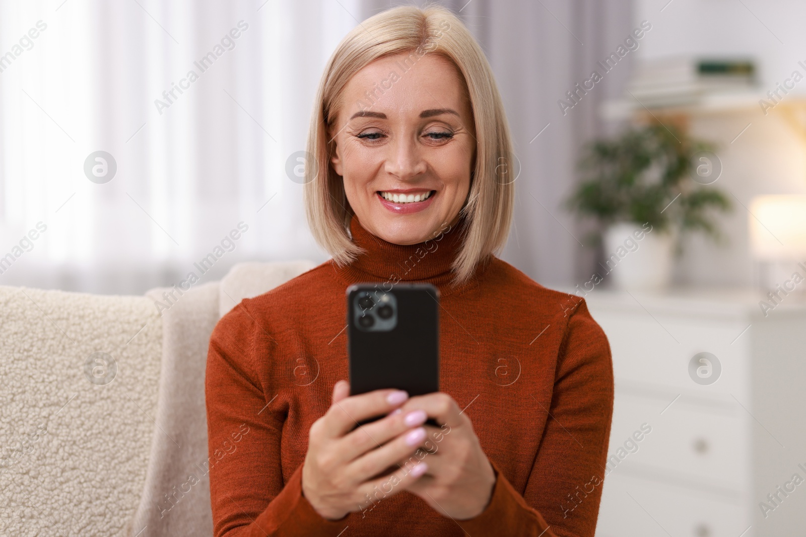 Photo of Portrait of smiling middle aged woman using smartphone at home