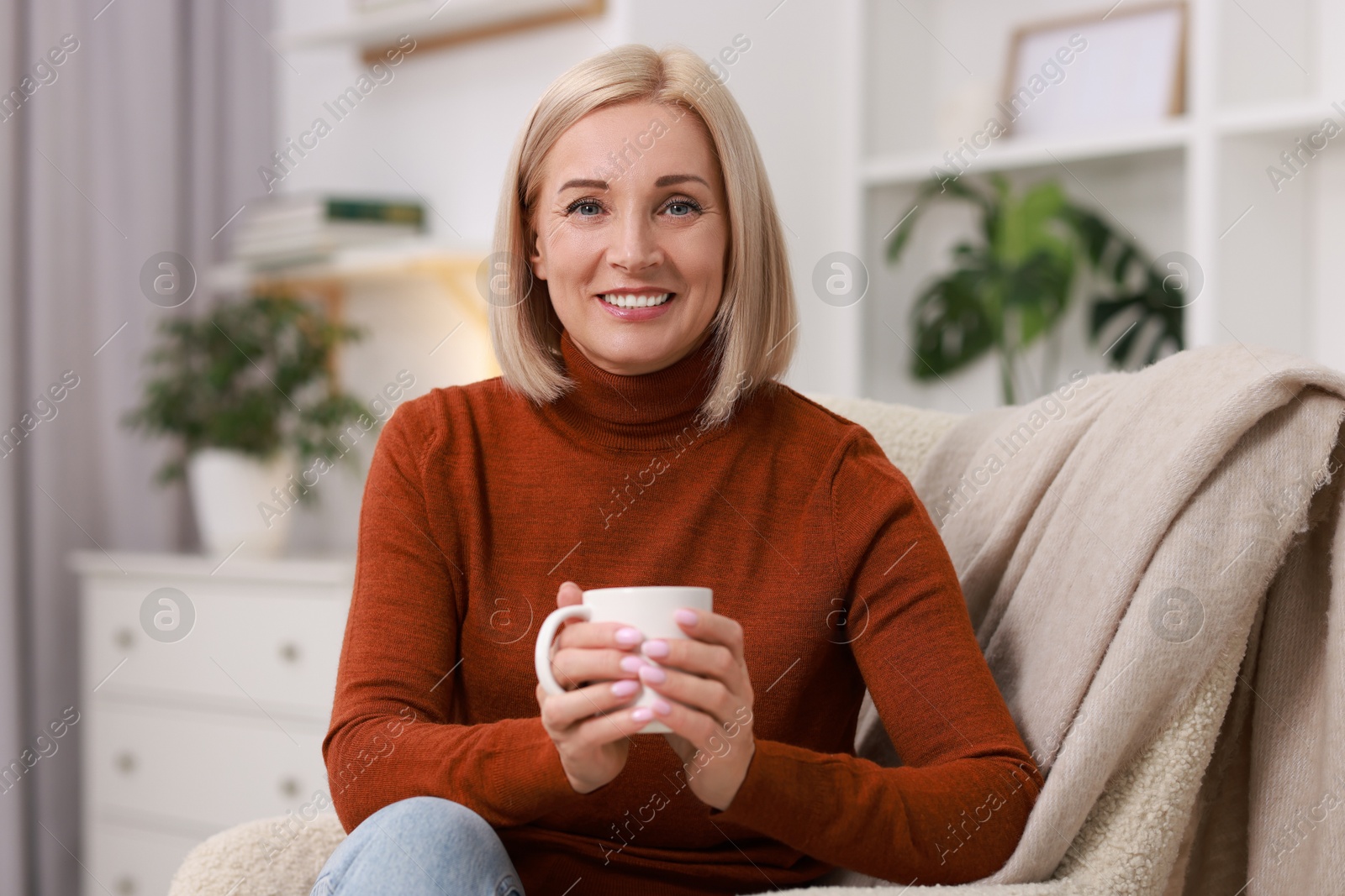 Photo of Smiling middle aged woman with cup of hot drink on armchair at home