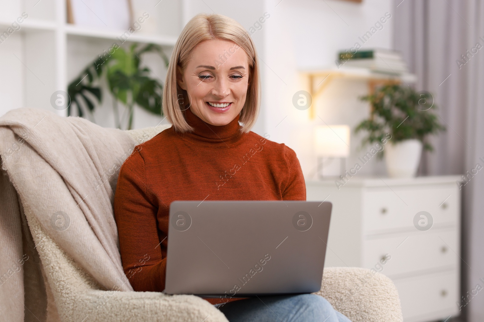 Photo of Portrait of smiling middle aged woman with laptop on armchair at home