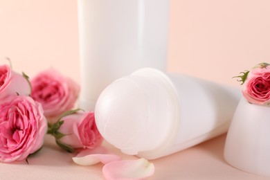 Photo of Different deodorants and beautiful rose flowers on beige background, closeup