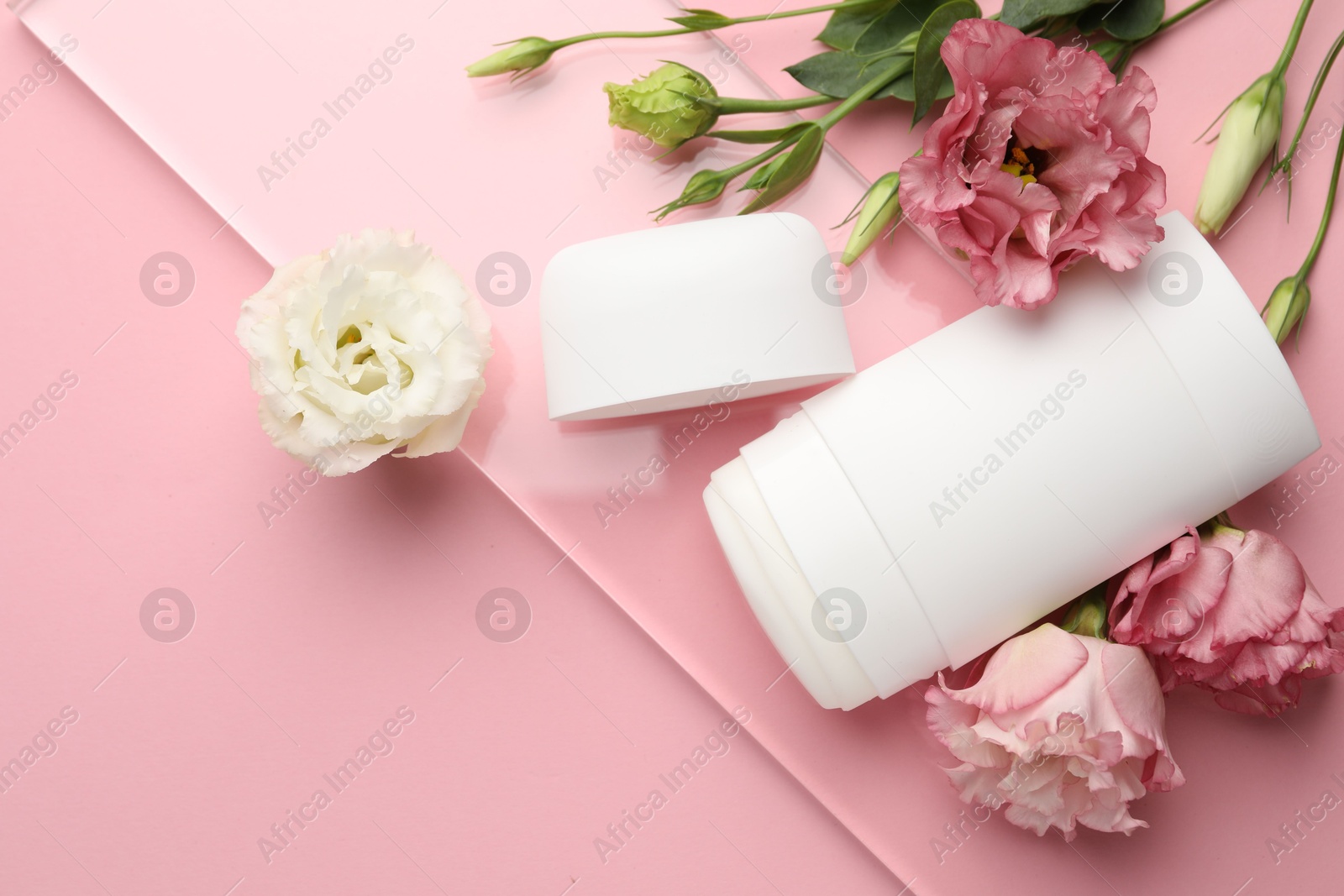 Photo of Solid deodorant and beautiful eustoma flowers on pink background, top view