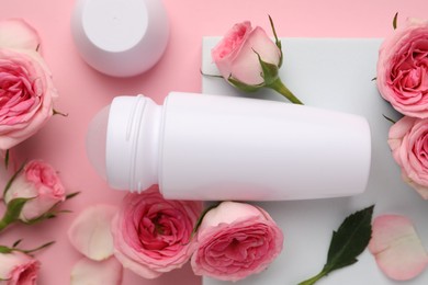 Photo of Roll-on deodorant and beautiful rose flowers on pink background, flat lay