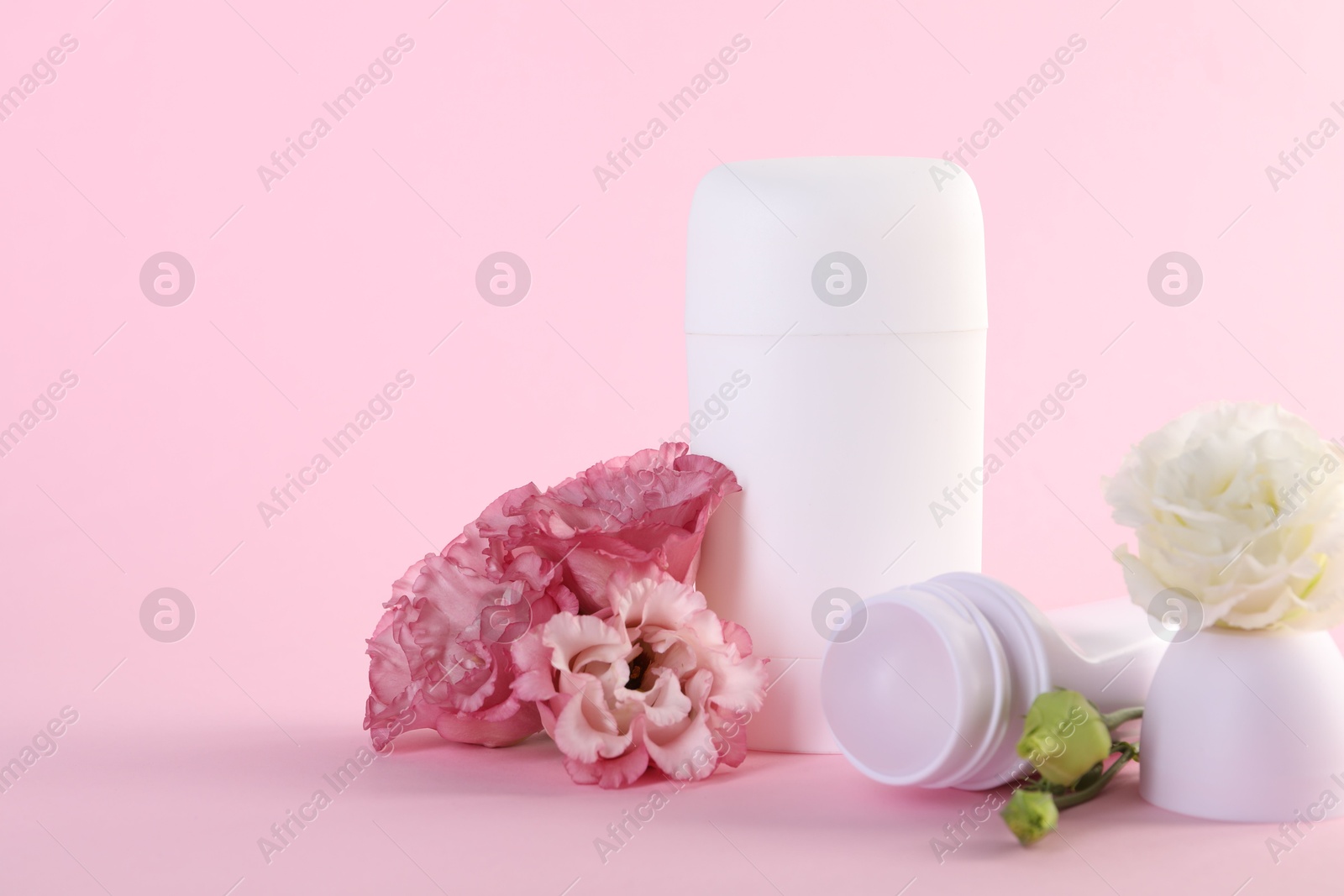 Photo of Different deodorants and beautiful eustoma flowers on pink background