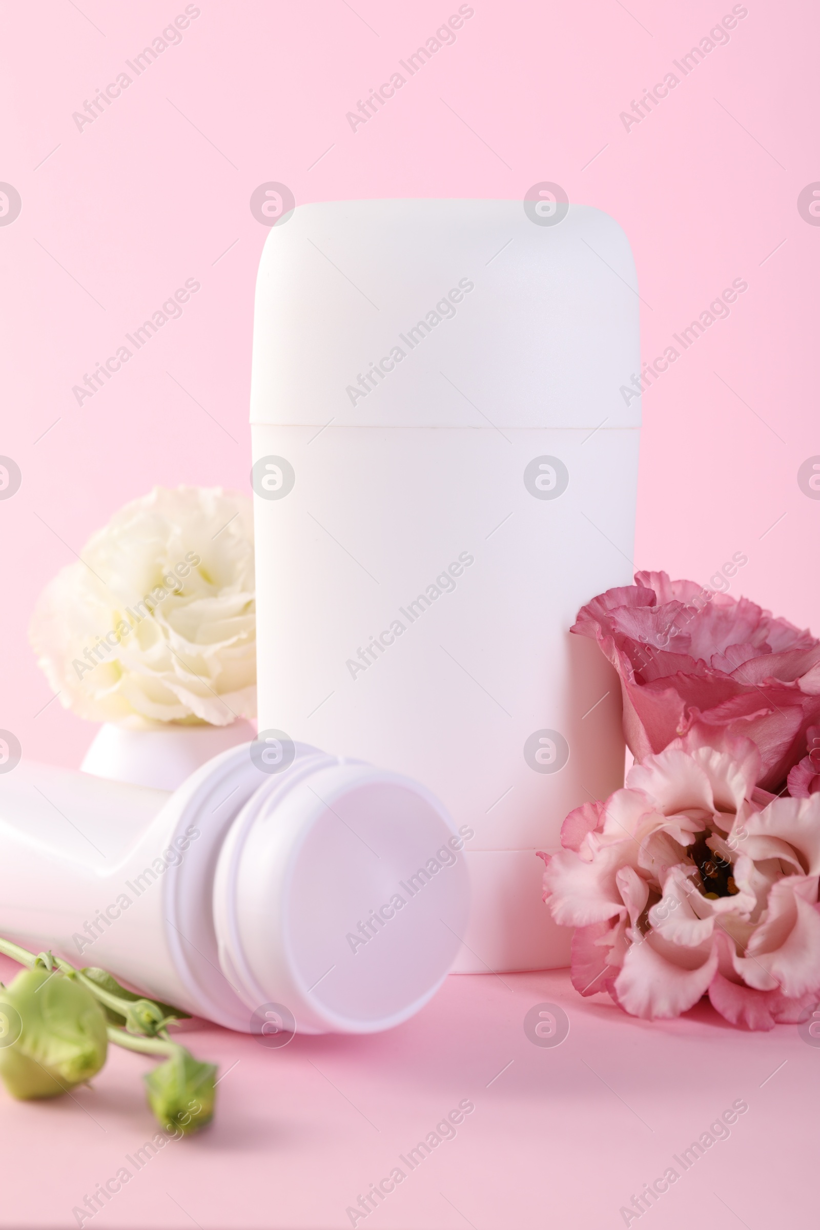 Photo of Different deodorants and beautiful eustoma flowers on pink background