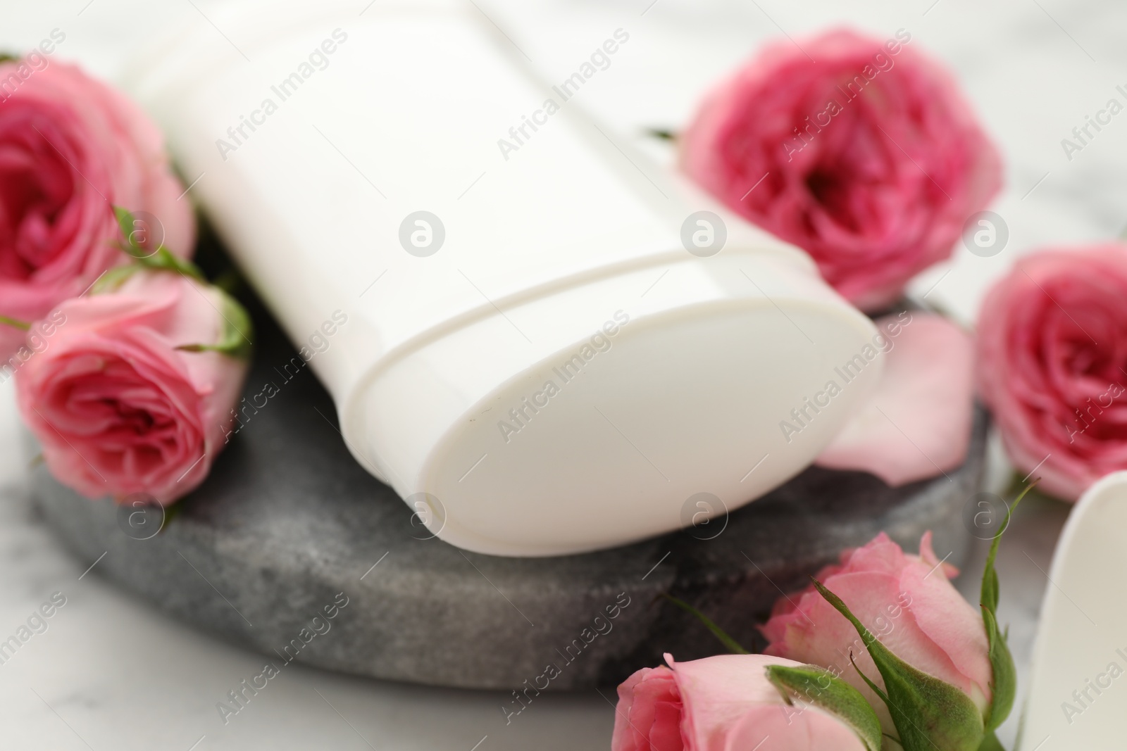 Photo of Solid deodorant and beautiful rose flowers on table, closeup