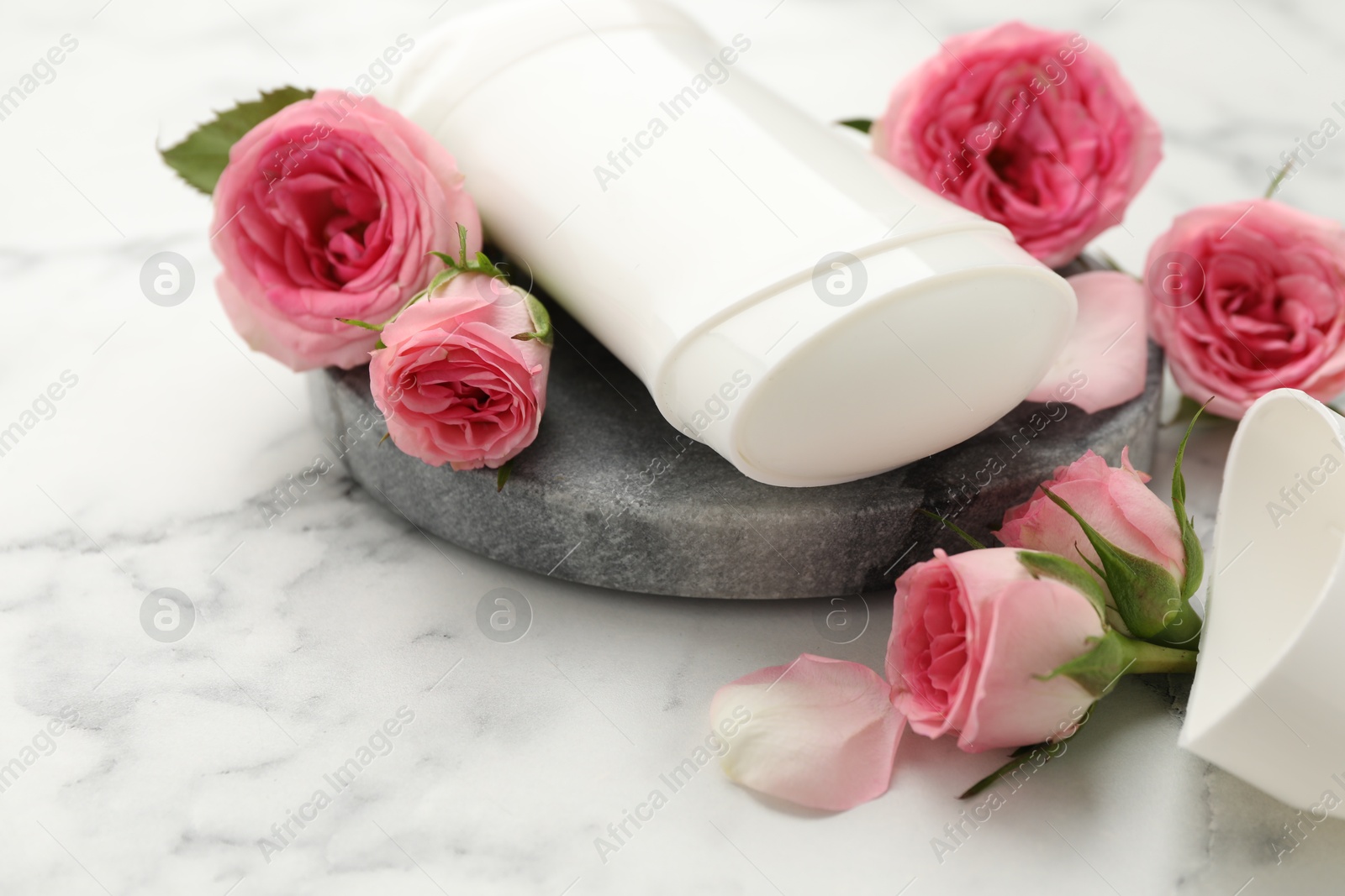 Photo of Solid deodorant and beautiful rose flowers on white marble table