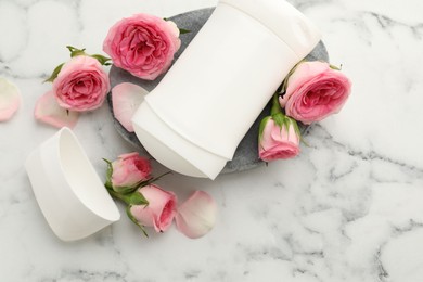 Photo of Solid deodorant and beautiful rose flowers on white marble table, top view