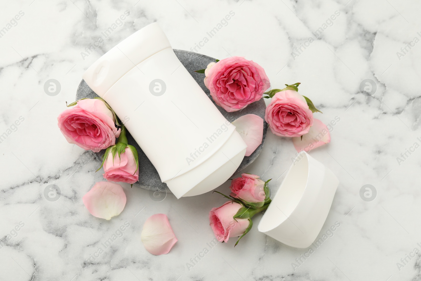 Photo of Solid deodorant and beautiful rose flowers on white marble table, flat lay