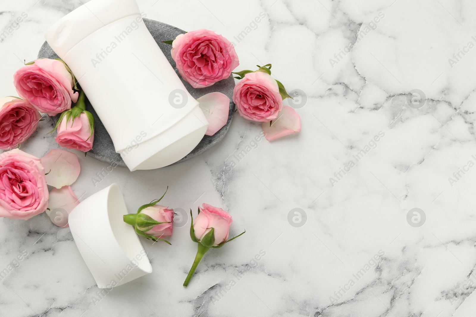 Photo of Solid deodorant and beautiful rose flowers on white marble table, flat lay. Space for text