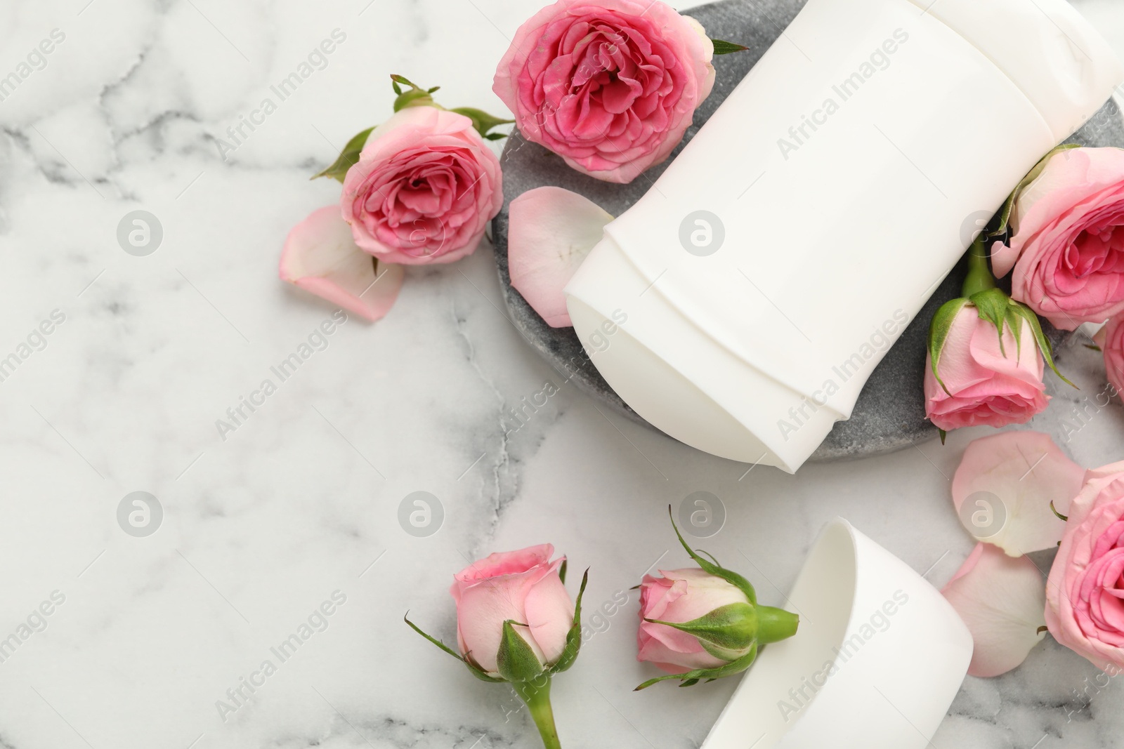 Photo of Solid deodorant and beautiful rose flowers on white marble table, flat lay. Space for text