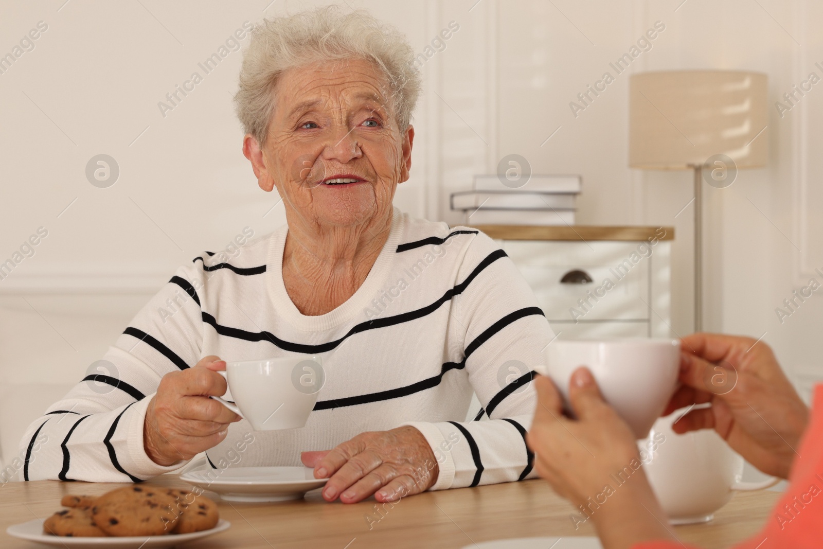 Photo of Caregiver and senior woman enjoying hot drink at table indoors