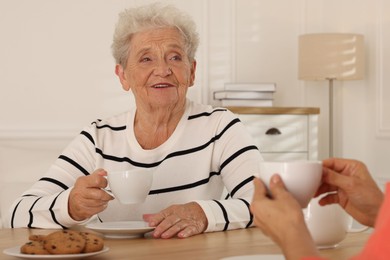 Caregiver and senior woman enjoying hot drink at table indoors