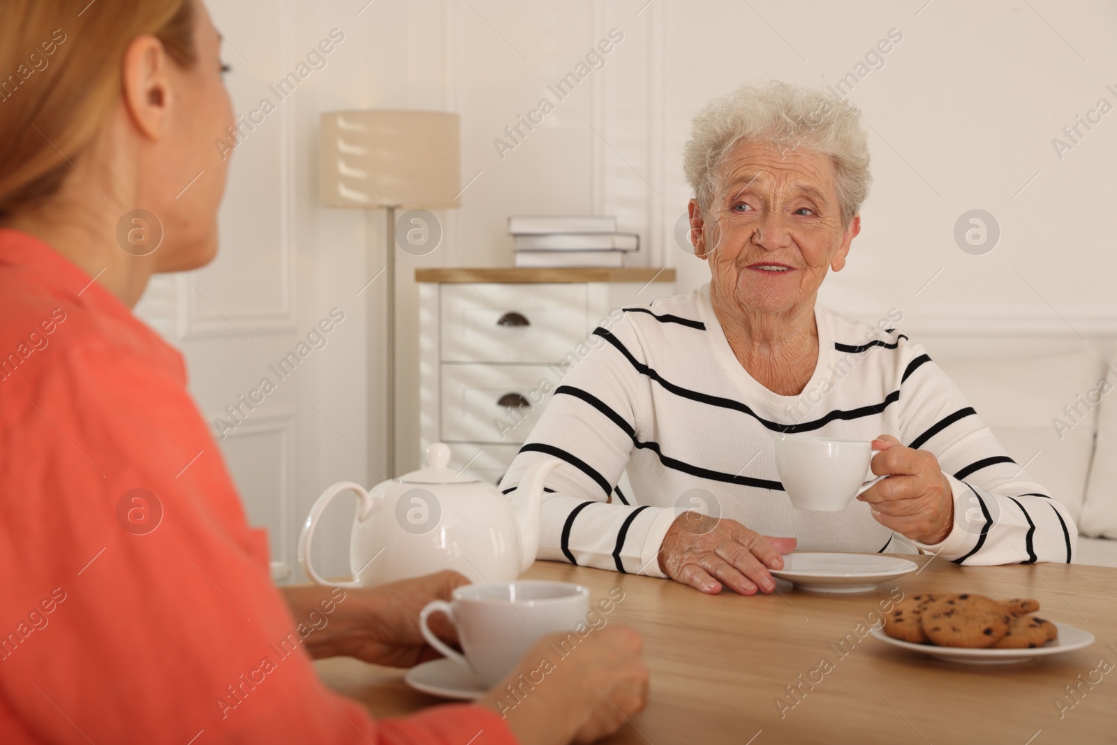 Photo of Caregiver and senior woman enjoying hot drink at table indoors