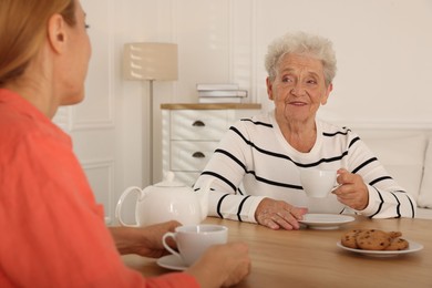 Photo of Caregiver and senior woman enjoying hot drink at table indoors