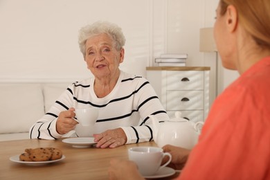 Photo of Caregiver and senior woman enjoying hot drink at table indoors