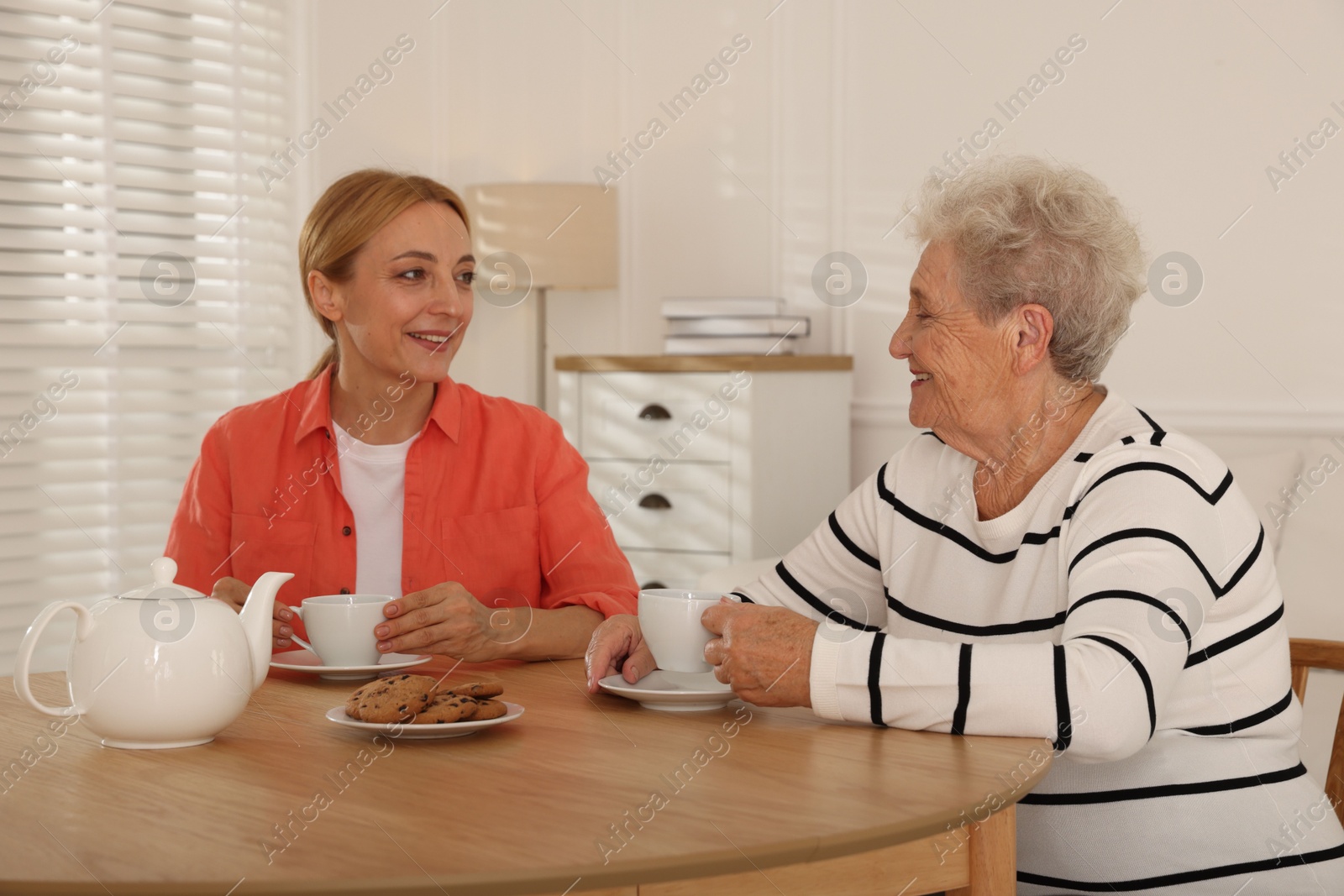 Photo of Caregiver and senior woman enjoying hot drink at table indoors