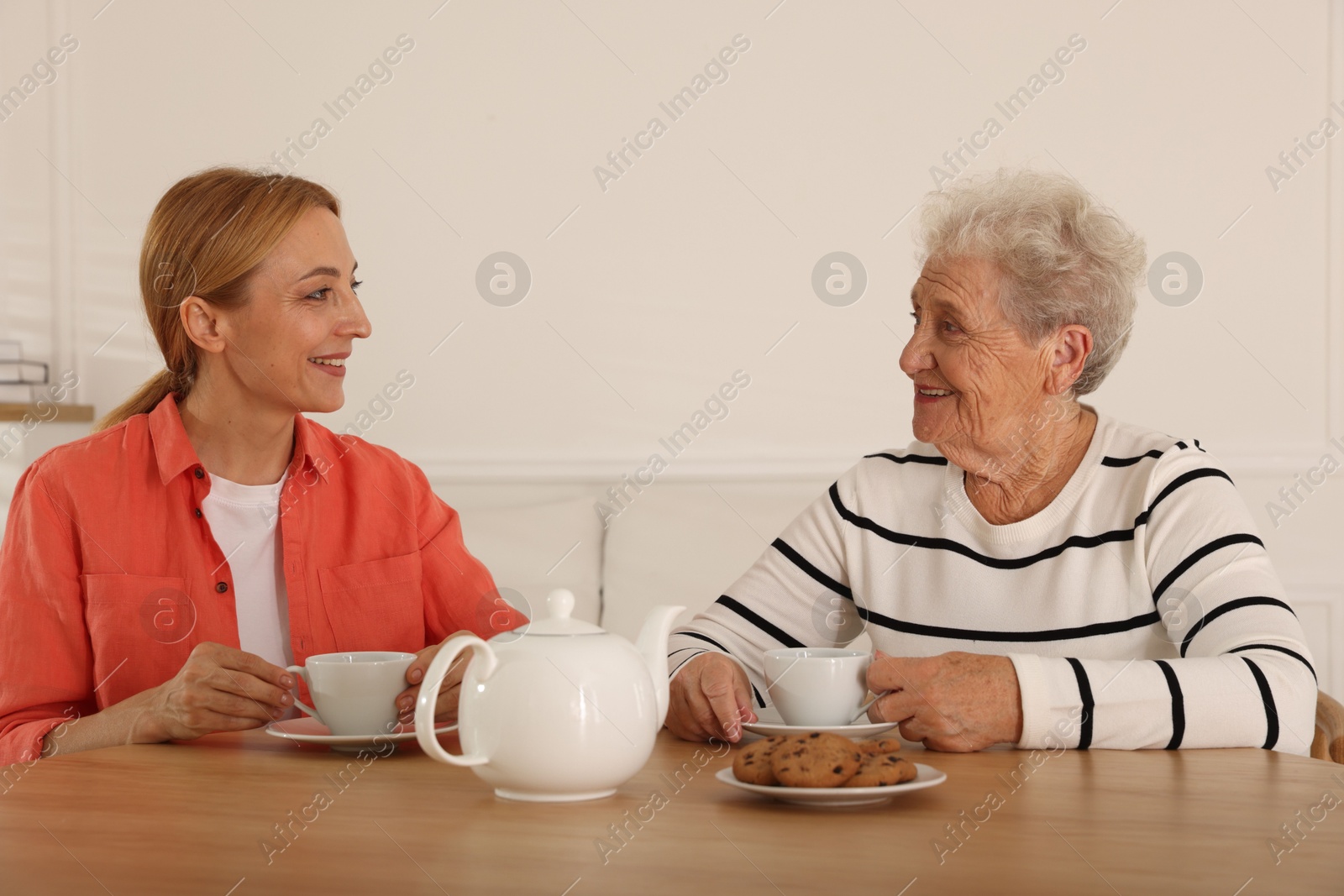 Photo of Caregiver and senior woman enjoying hot drink at table indoors