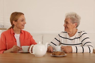 Photo of Caregiver and senior woman enjoying hot drink at table indoors