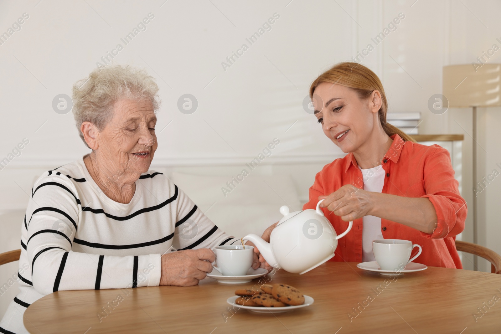 Photo of Caregiver and senior woman enjoying hot drink at table indoors