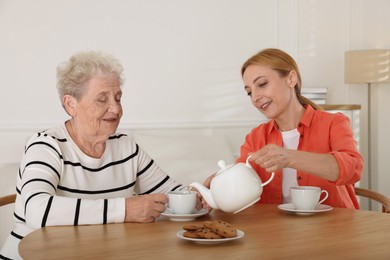 Photo of Caregiver and senior woman enjoying hot drink at table indoors