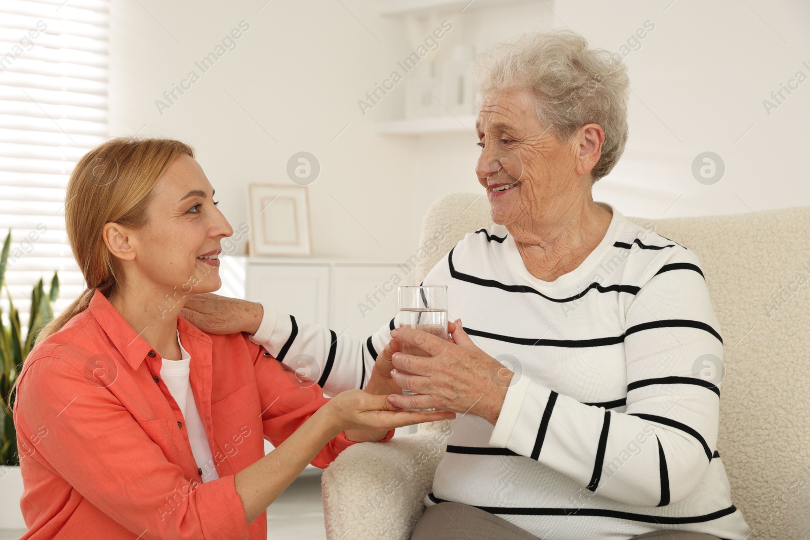 Photo of Caregiver giving glass of water to senior woman at home