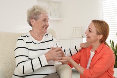 Caregiver giving glass of water to senior woman at home