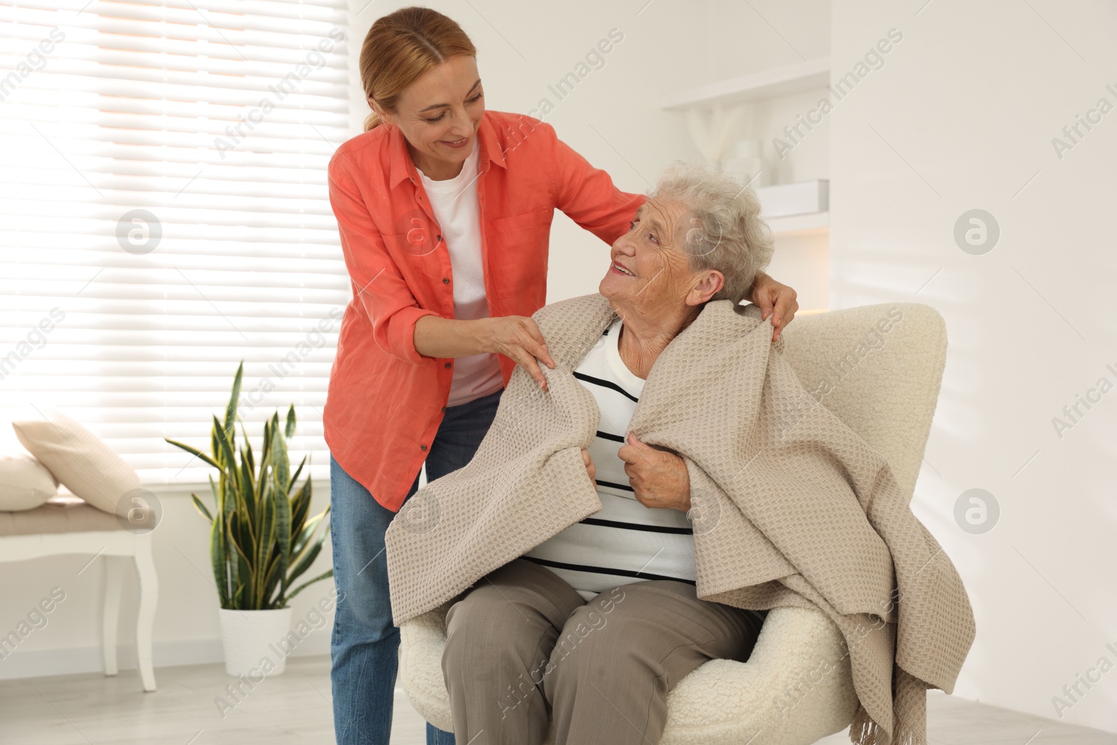 Photo of Caregiver covering senior woman with blanket at home