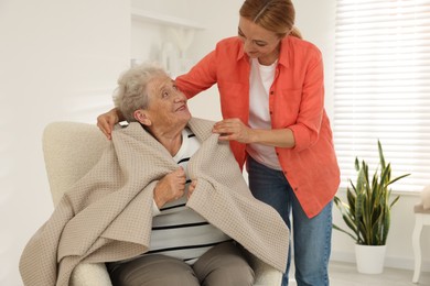 Photo of Caregiver covering senior woman with blanket at home