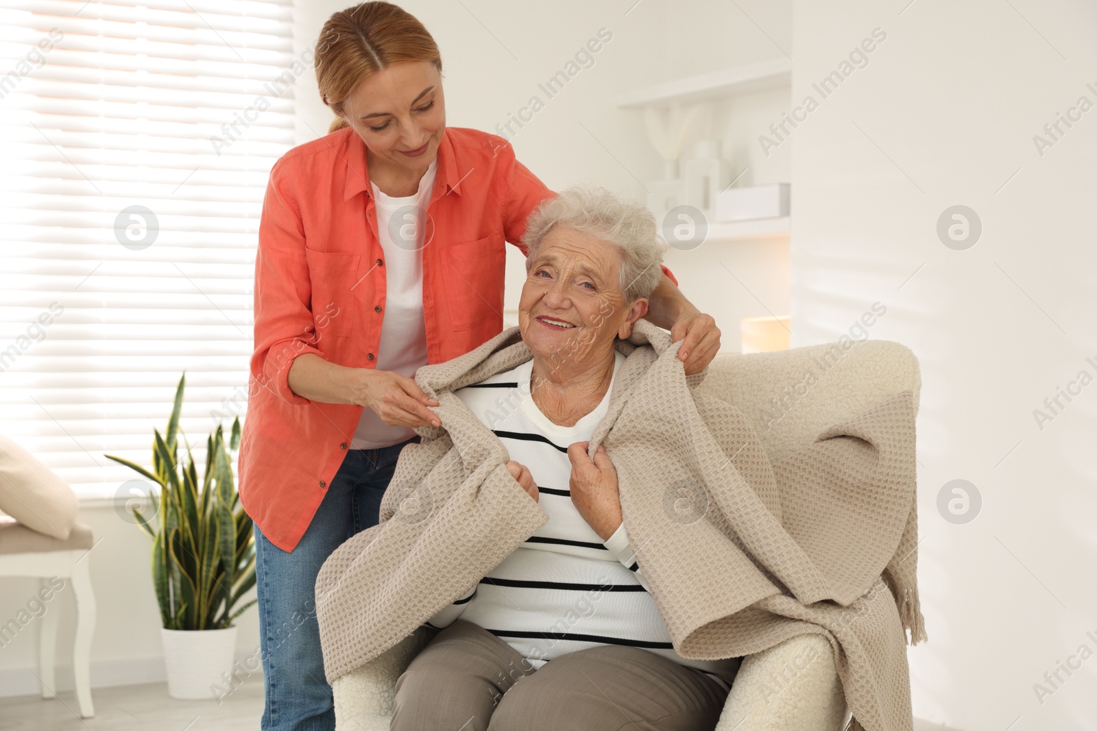 Photo of Caregiver covering senior woman with blanket at home