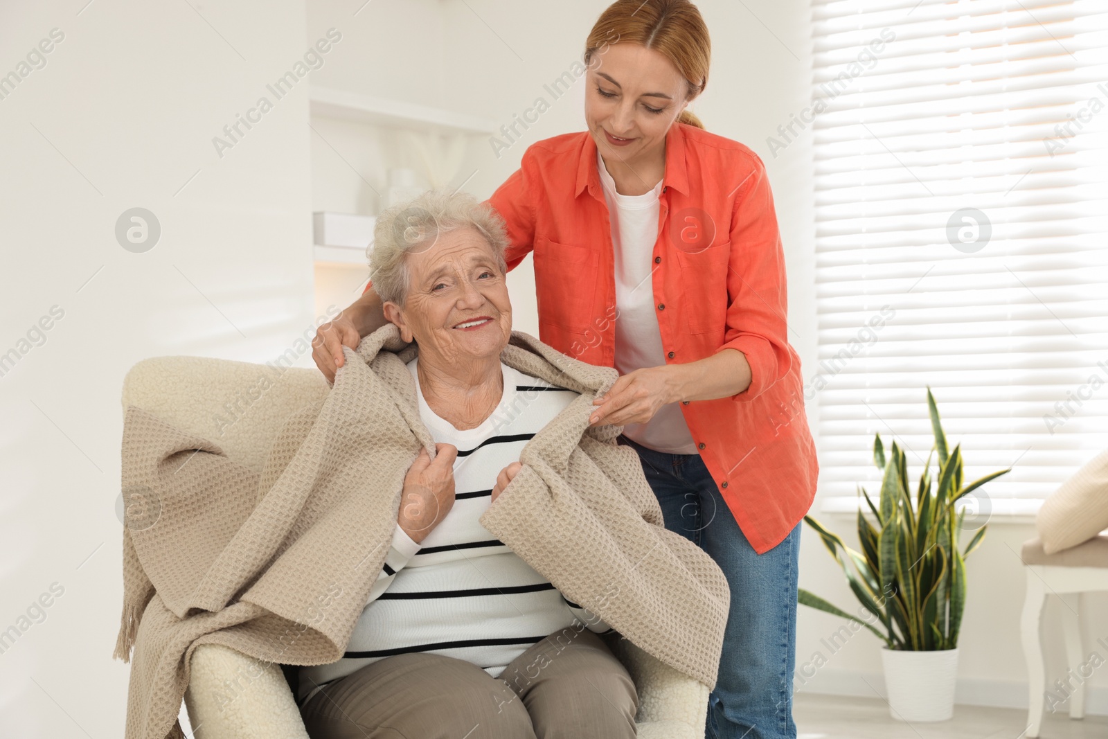 Photo of Caregiver covering senior woman with blanket at home