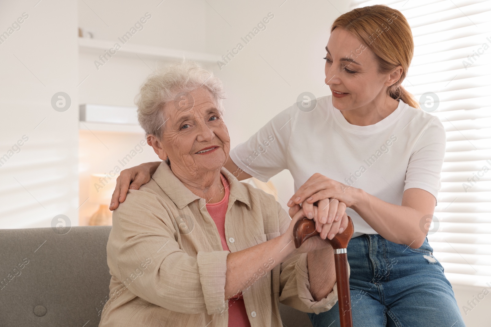 Photo of Caregiver supporting senior woman in living room at home