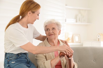 Caregiver supporting senior woman in living room at home