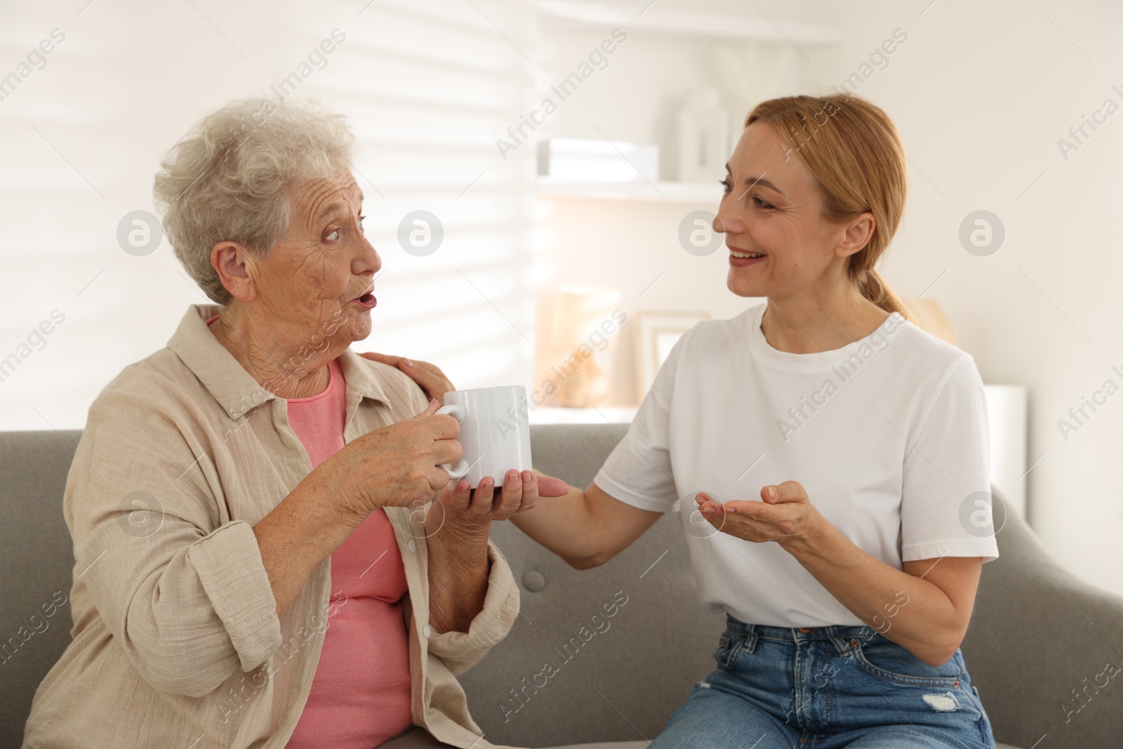 Photo of Caregiver supporting senior woman on sofa at home