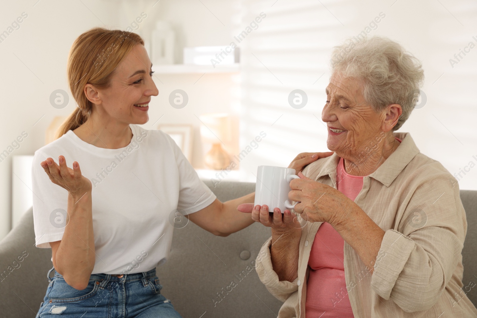 Photo of Caregiver supporting senior woman on sofa at home