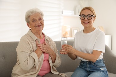 Photo of Caregiver giving glass of water to senior woman at home