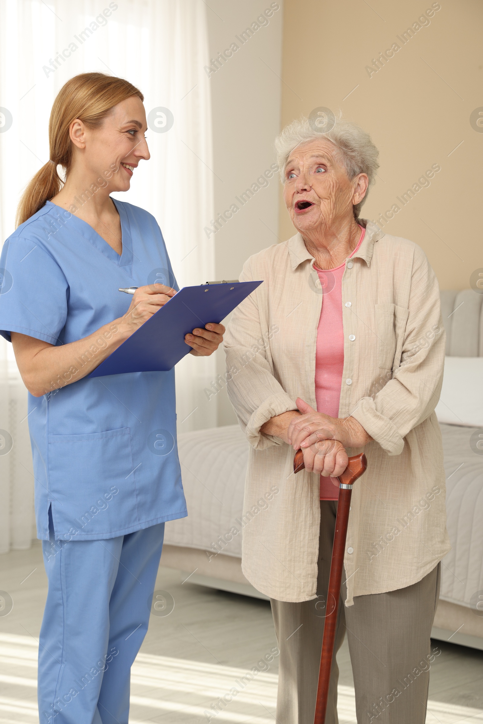 Photo of Healthcare worker with clipboard consulting senior woman indoors