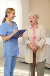 Photo of Healthcare worker with clipboard consulting senior woman indoors