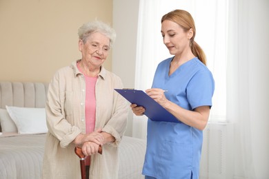 Photo of Healthcare worker with clipboard consulting senior woman indoors