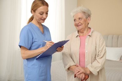 Photo of Healthcare worker with clipboard consulting senior woman indoors