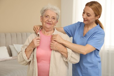 Photo of Healthcare worker helping senior woman to put on jacket at home