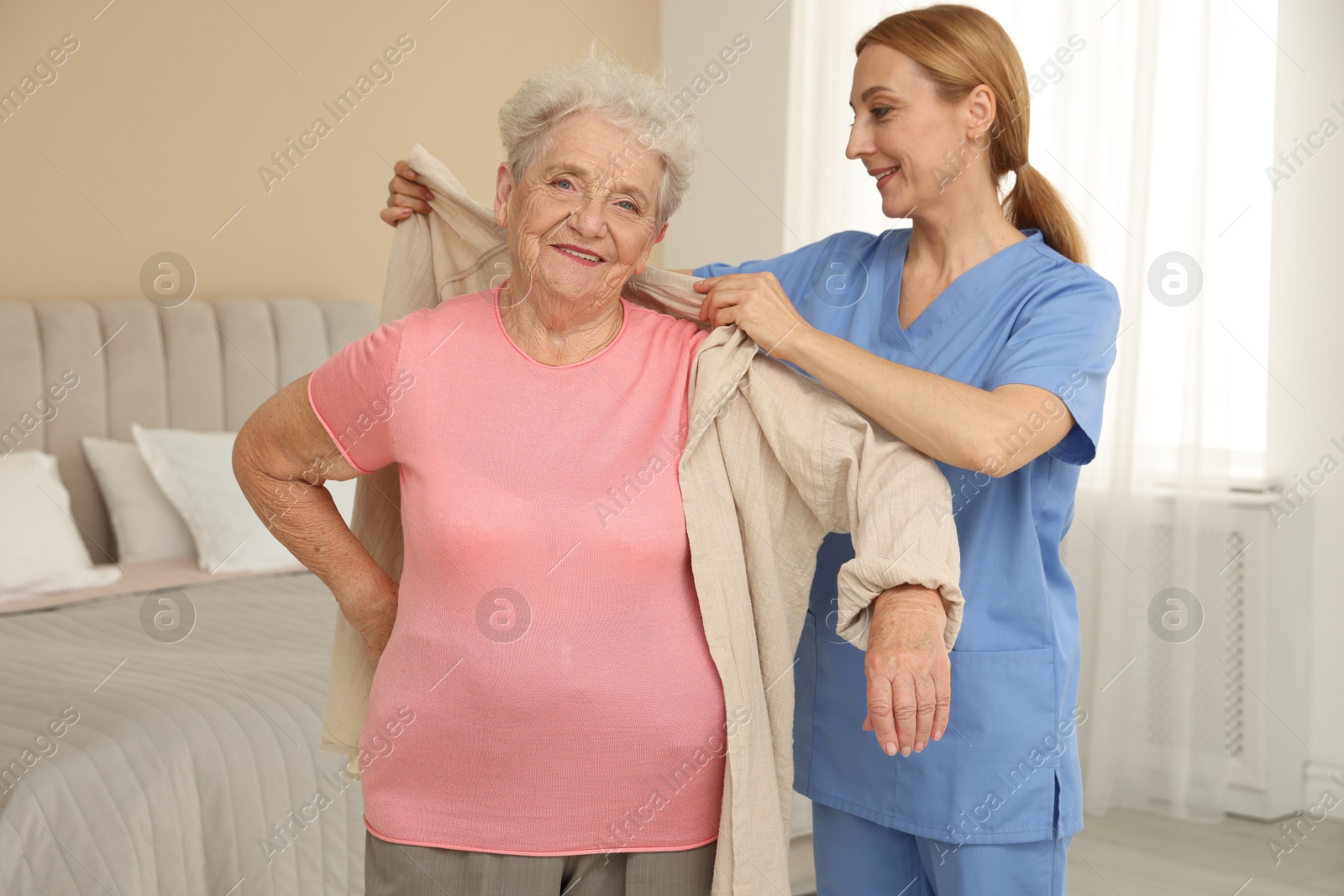 Photo of Healthcare worker helping senior woman to put on jacket at home