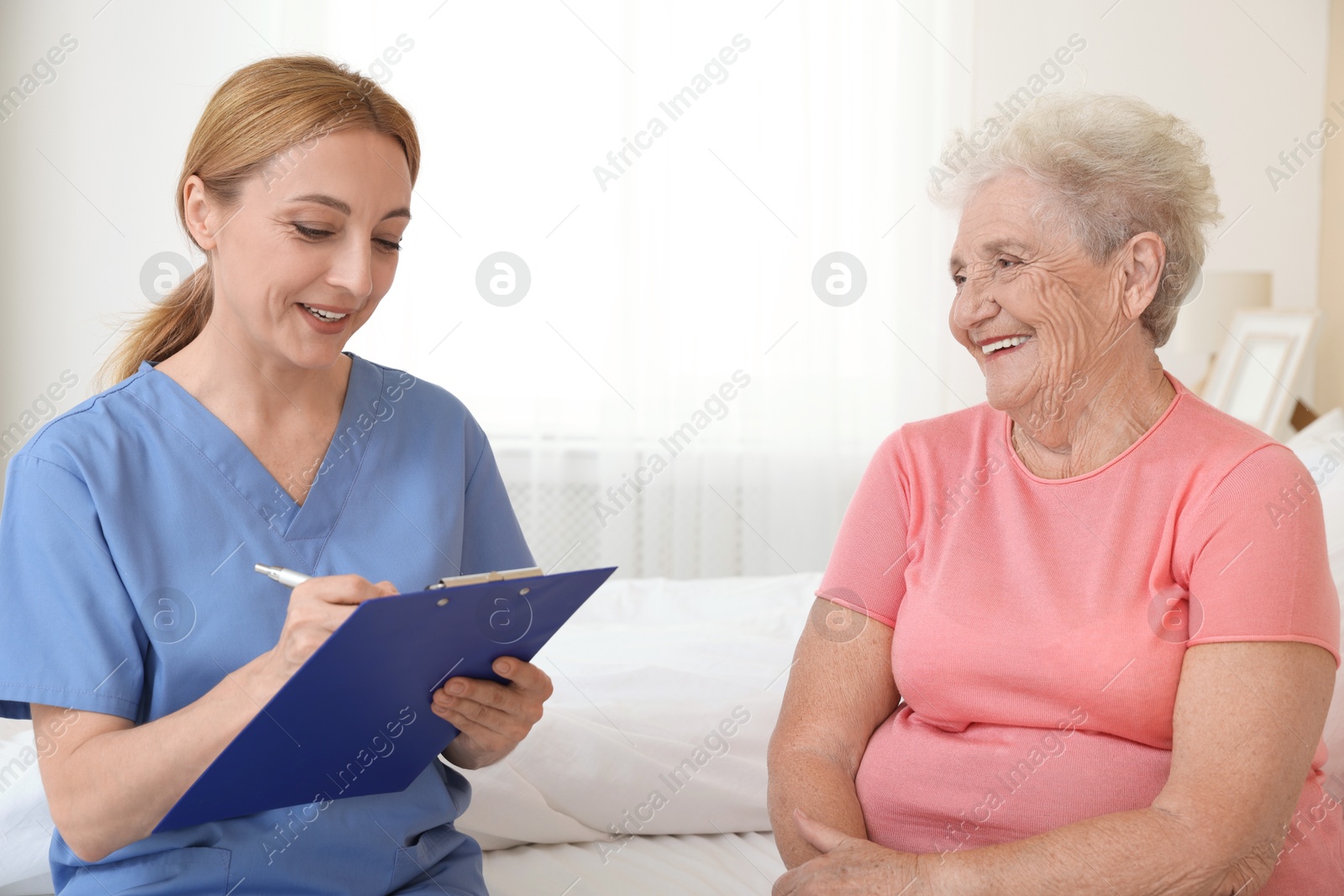 Photo of Healthcare worker with clipboard consulting senior patient on bed indoors