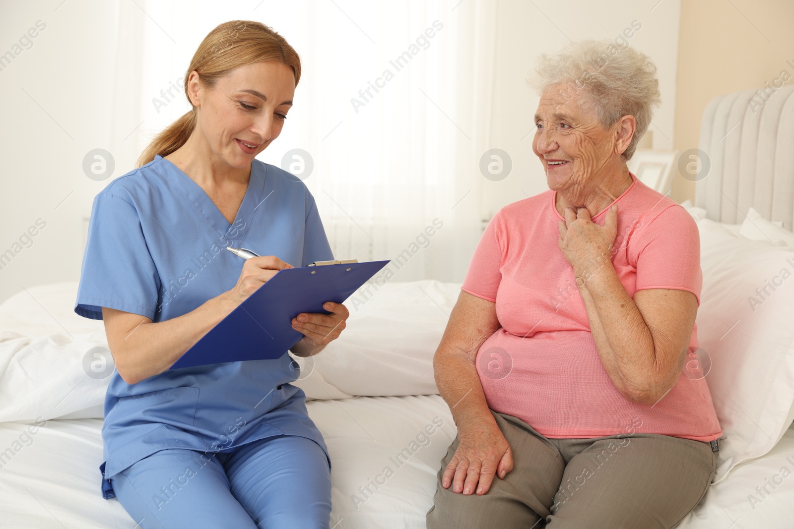 Photo of Healthcare worker with clipboard consulting senior patient on bed indoors