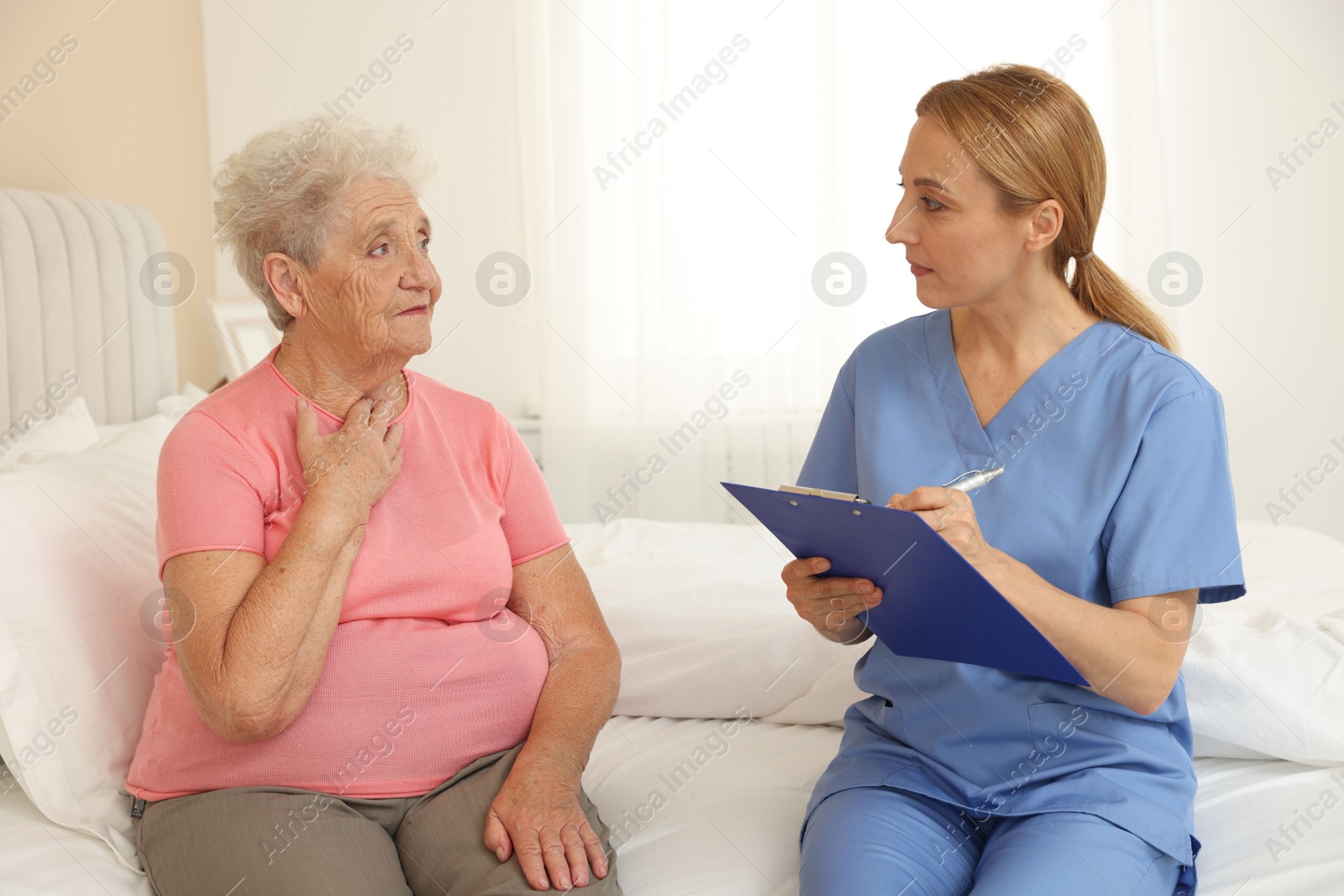 Photo of Healthcare worker with clipboard consulting senior patient on bed indoors