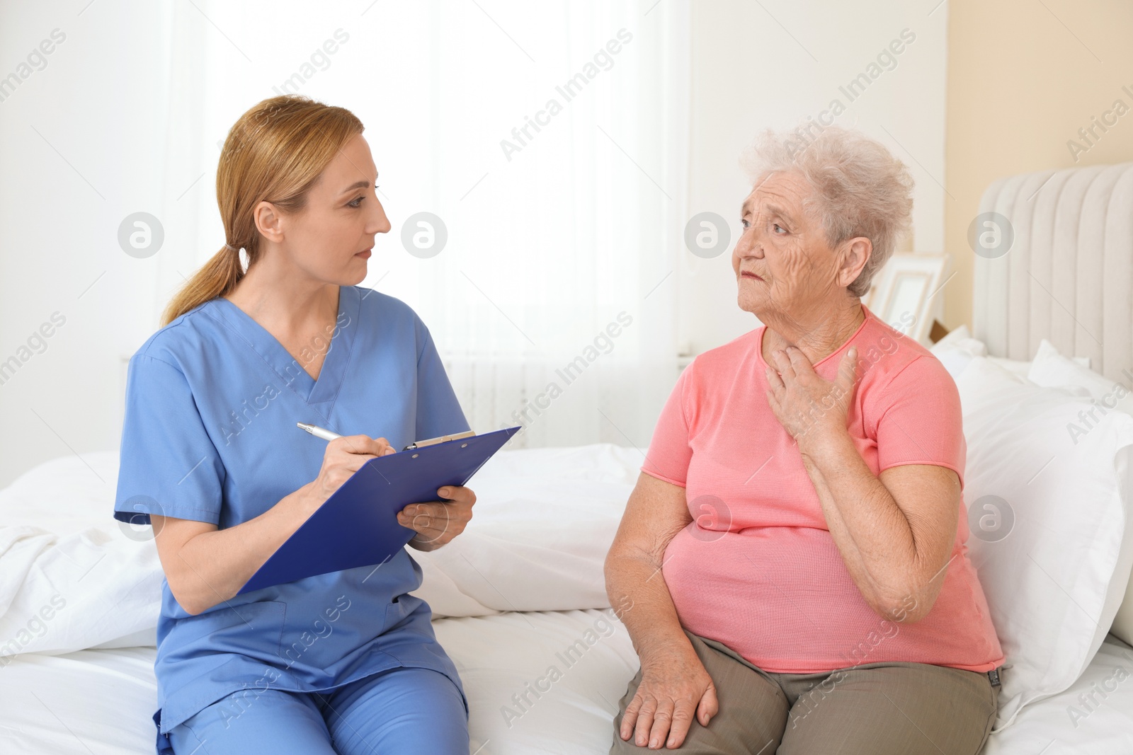 Photo of Healthcare worker with clipboard consulting senior patient on bed indoors