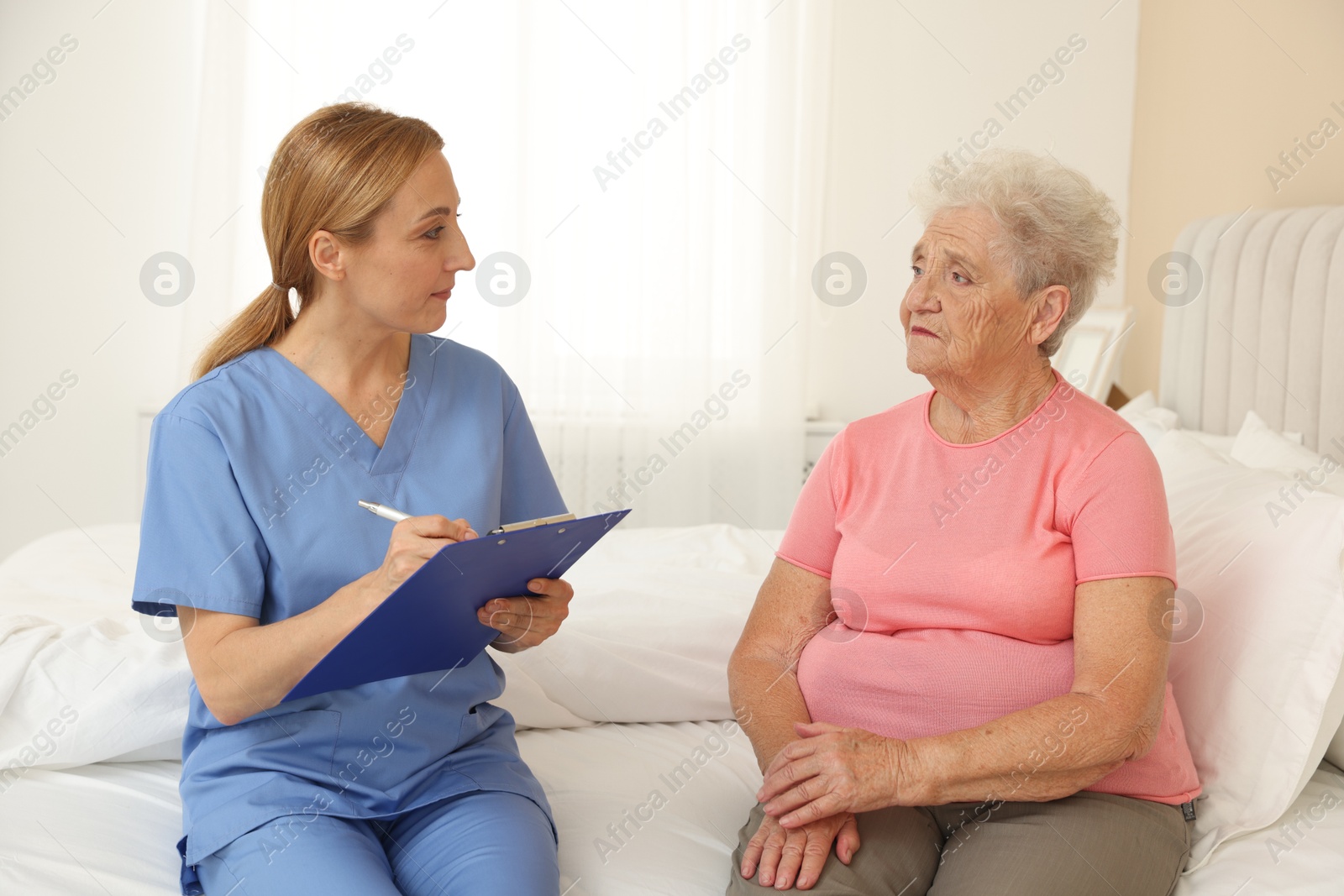 Photo of Healthcare worker with clipboard consulting senior patient on bed indoors