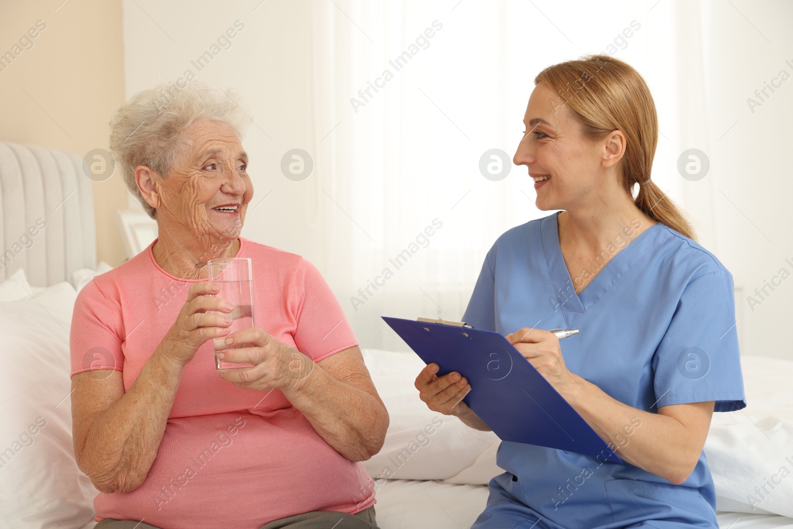 Photo of Healthcare worker with clipboard consulting senior patient on bed indoors