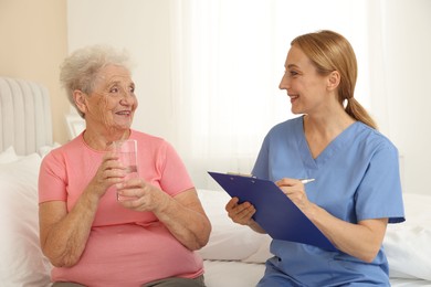 Healthcare worker with clipboard consulting senior patient on bed indoors