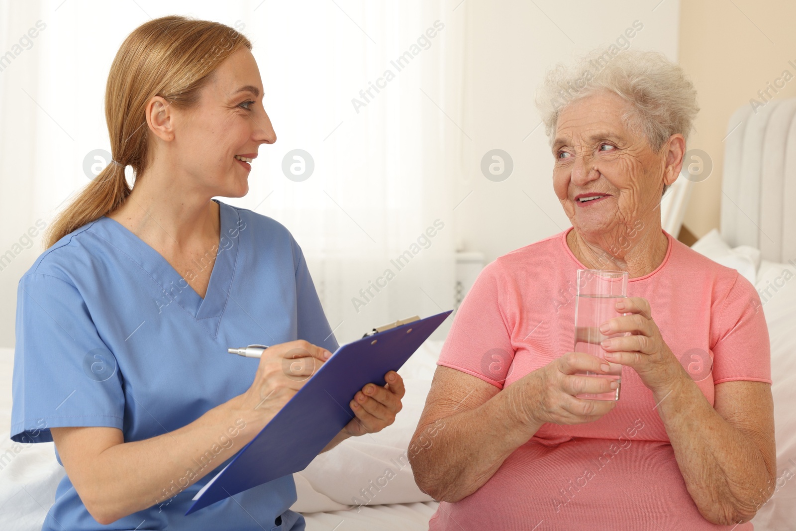 Photo of Healthcare worker with clipboard consulting senior patient on bed indoors