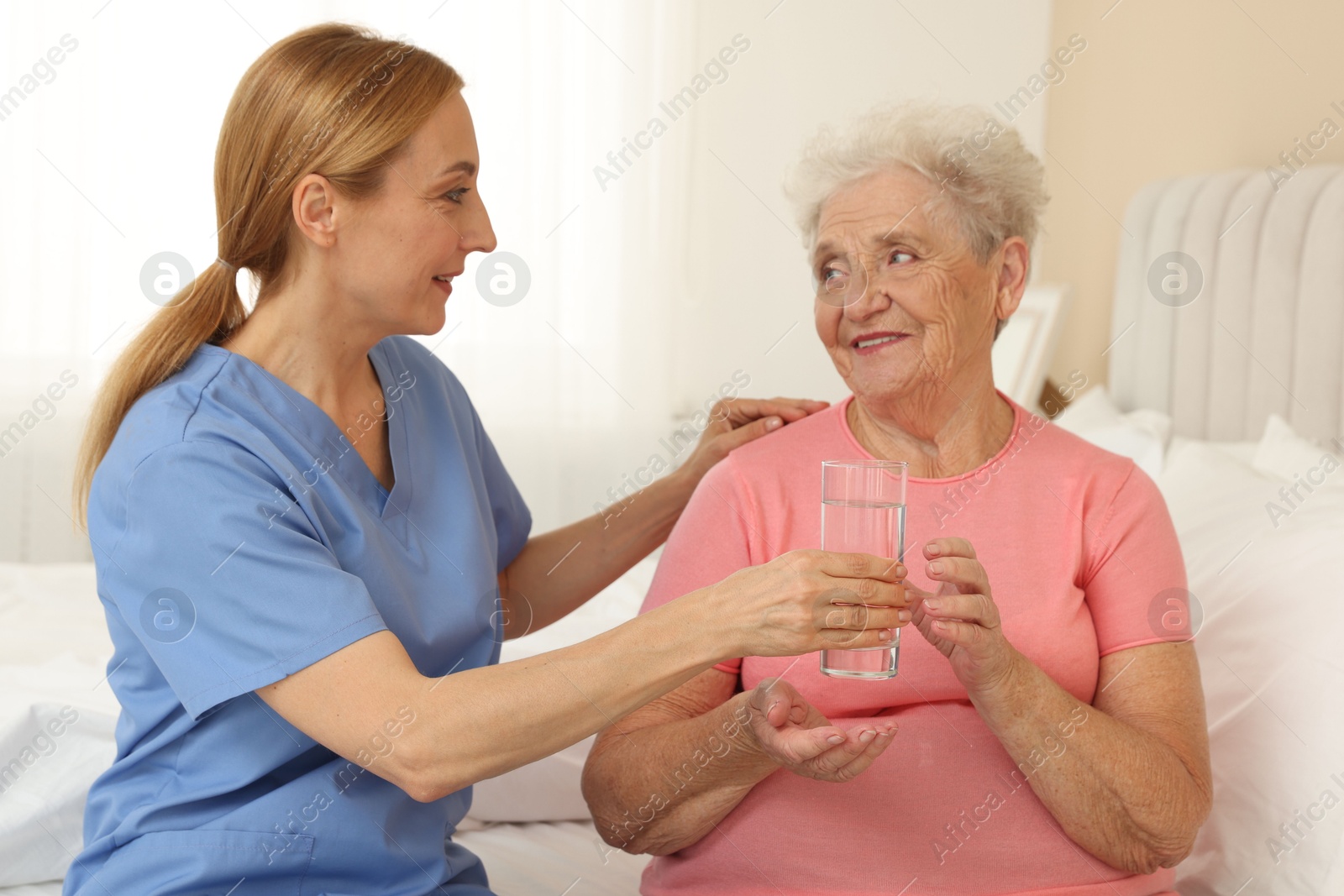 Photo of Healthcare worker giving glass of water to senior patient at home